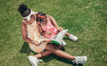 mother and daughter sit on grass reading a book