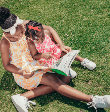 mother and daughter sit on grass reading a book