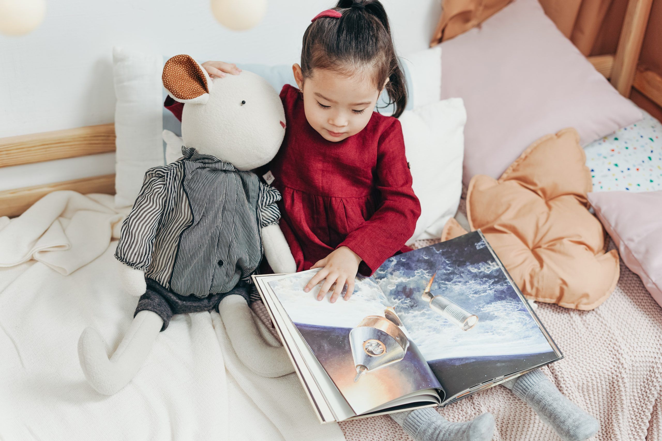 toddler sitting on bed with stuffed animal looking at a picture book