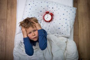 boy holding his ears with alarm clock beside him on pillow