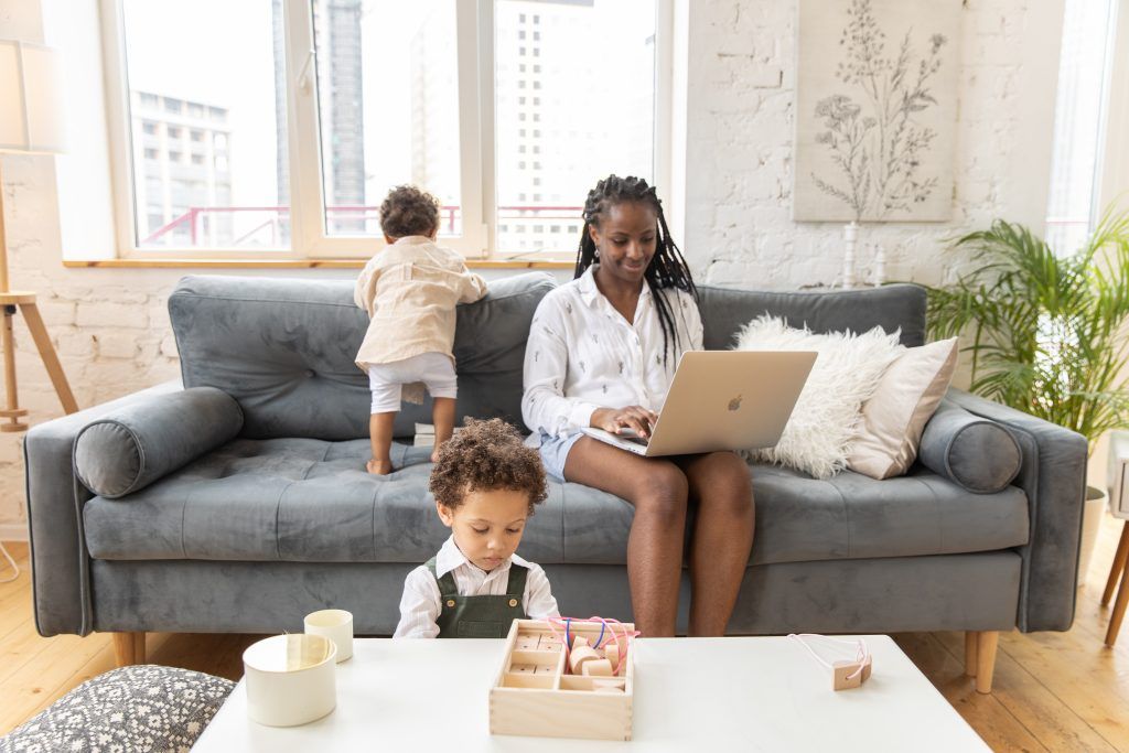 woman sitting on couch with laptop in lap while baby and toddler play