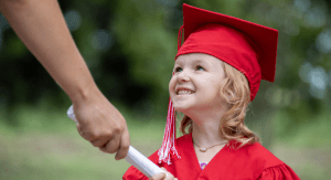 preschool girl in cap and gown accepts diploma