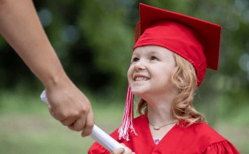 preschool girl in cap and gown accepts diploma