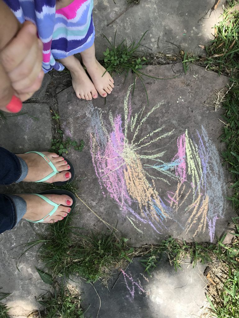 woman and child's feet are shown beside a child's sidewalk chalk drawing