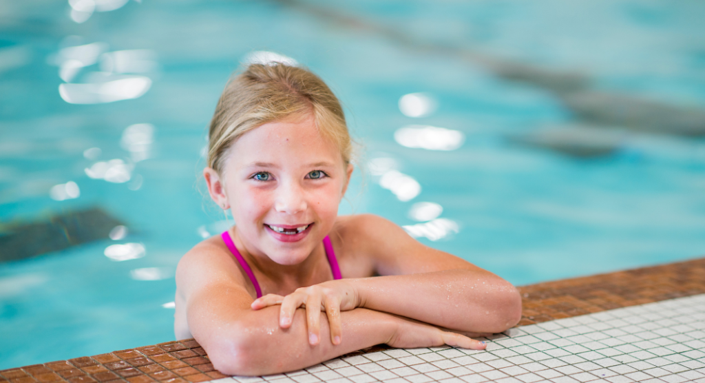 girl smiling while holding onto side of pool