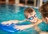 A Moms’ Guide to Swim Lessons in Houston child with goggles looks at swim instructor while holding on to kickboard