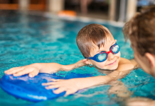 child with goggles looks at swim instructor while holding on to kickboard