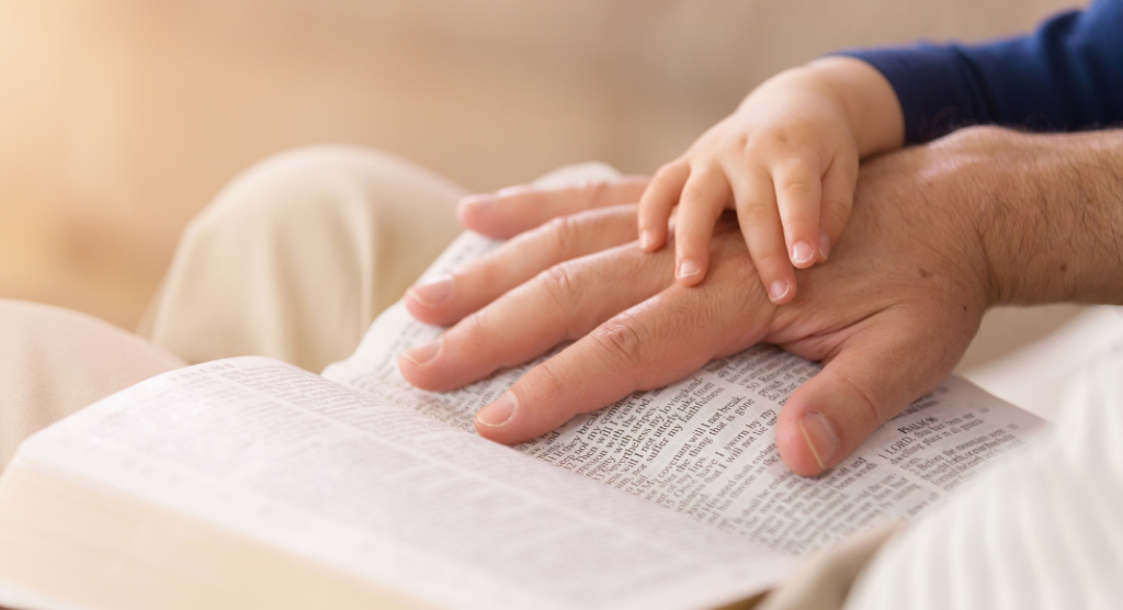 man's hand on a bible with child's hand covering it 