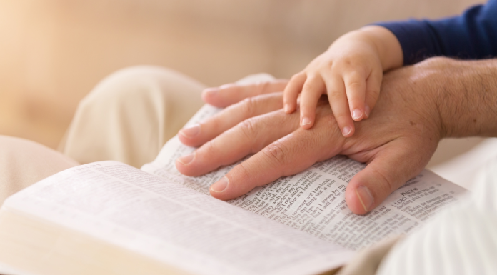 man's hand on a bible with child's hand covering it