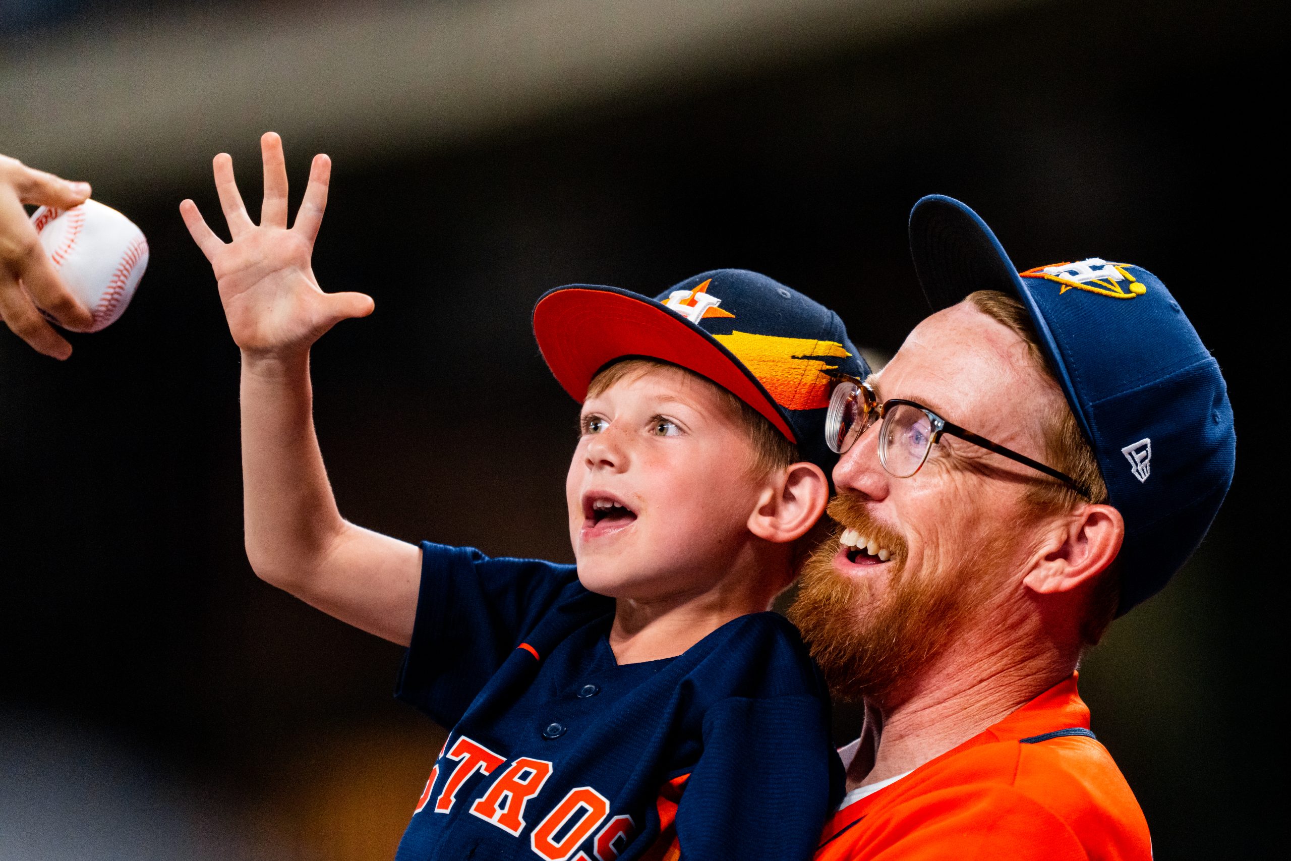 son being held by dad reaches for a baseball