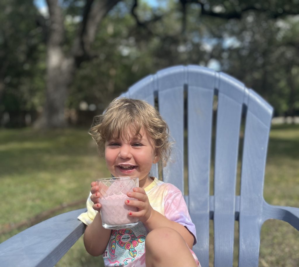 toddler sits outside drinking a smoothie