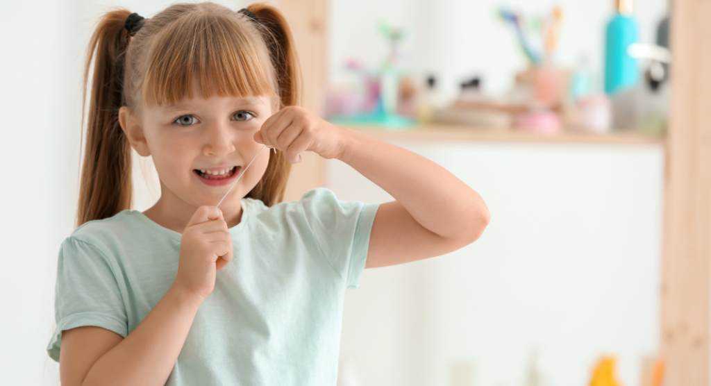 girl smiles as she holds up a piece of floss