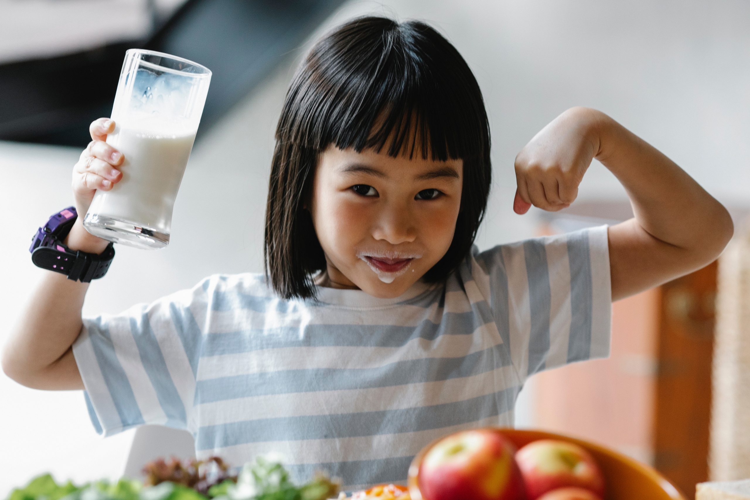girl with milk moustache holds glass of milk