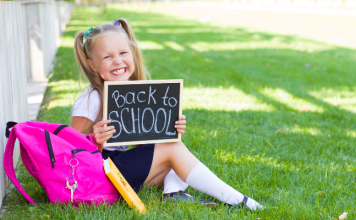 preschool girl sits on grass with Back to School sign and backpack