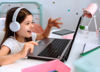 child participates in online schooling sitting at desk looking at computer with headphones on