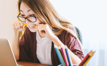 woman looking at laptop while chewing on pencil
