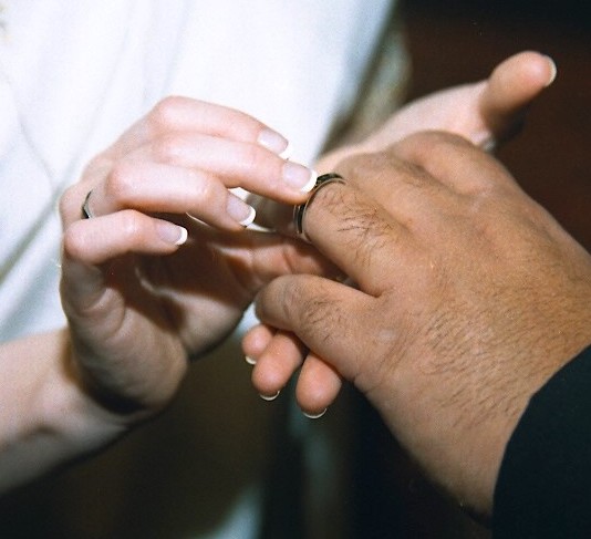 woman's hand slipping wedding ring on man's finger