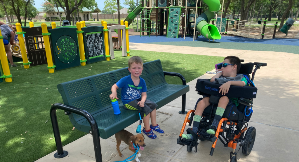 child in wheelchair and preschooler at accessible playground