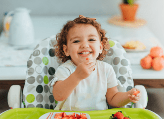 toddler sits in high chair eating strawberries