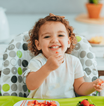 toddler sits in high chair eating strawberries