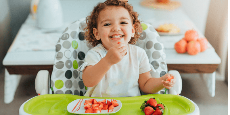 child sits in high chair eating strawberries