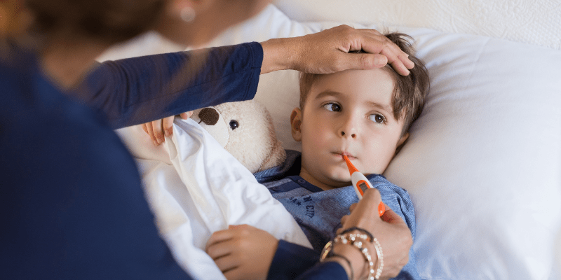child in bed with thermometer in mouth