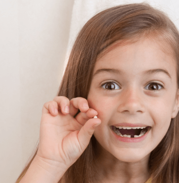 girl holds up lost tooth