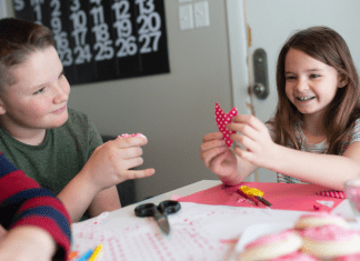 children sit at table making DIY class Valentines