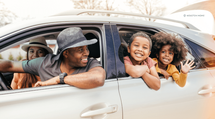 family of four with heads out the car windows, smiling