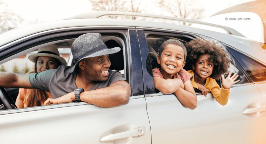 family of four with heads out window of car, smiling