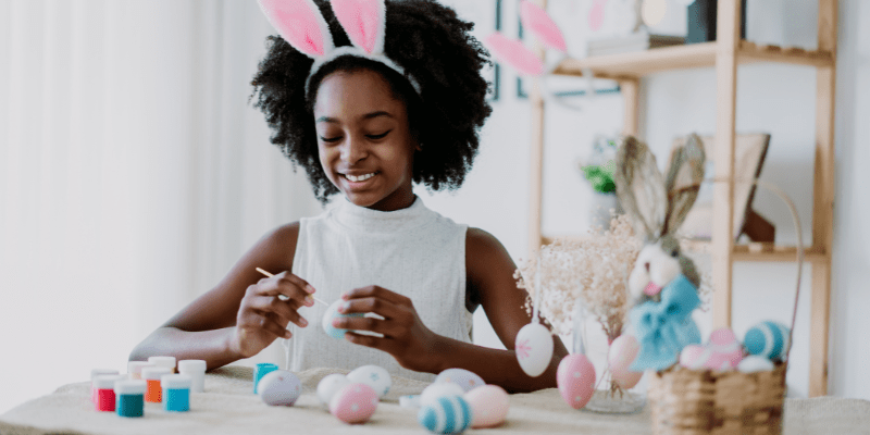 child wearing bunny ears headband paints eggs