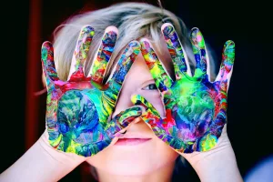 child holds up hands covered in paint