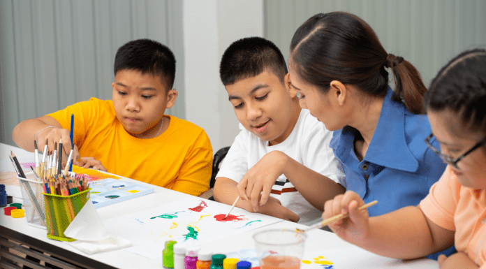 children sit at table painting