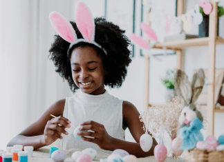 young girl wearing bunny ears paints Easter eggs