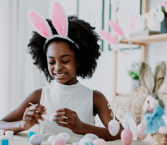 young girl wearing bunny ears paints Easter eggs