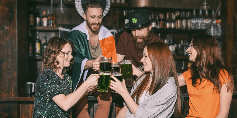 group of adults toast with mugs of green beer