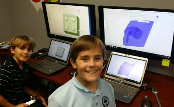 Two boys smile at their computers