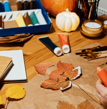 a table covered in leaves, paint, and a hand holding a paintbrush completing fall crafts