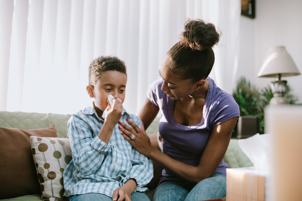 a mom comforts her son who is blowing his nose
