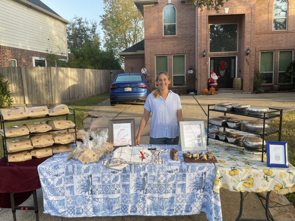 woman entrepreneur stands outside her home at a table with sourdough bread