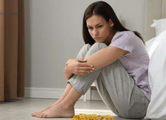 woman sits on floor sadly looking at scale