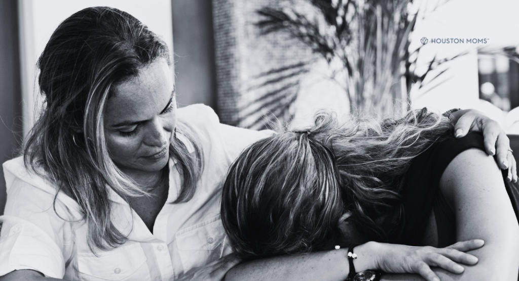 mother with arm around daughter whose head is on the table and is struggling with addiction
