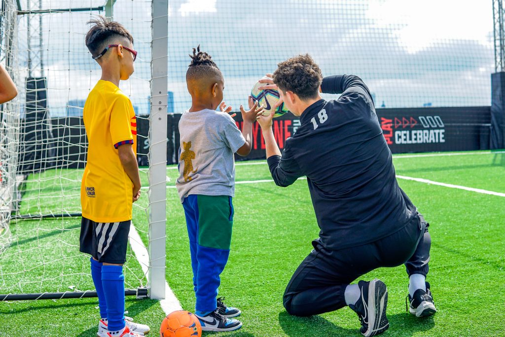 A coach shows two boys how to catch a soccer ball as goalie.
