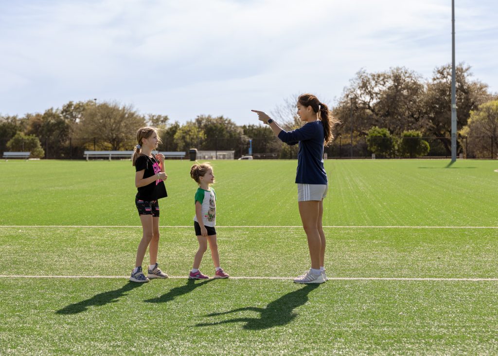 A woman coaches two kids on a soccer field
