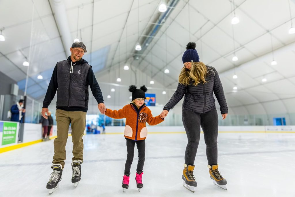 A mom and dad ice skating and holding hands with their child