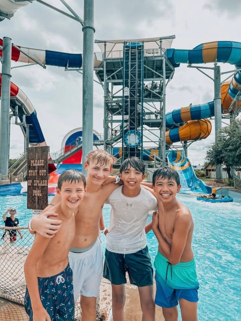 A group of boys smile in front of water slides