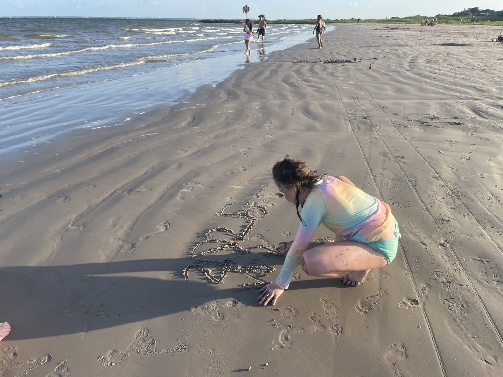girl crouched down drawing in sand