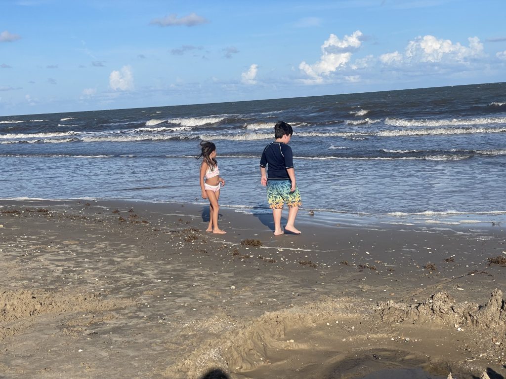 Elementary-aged children walking along the shoreline, watching the waves