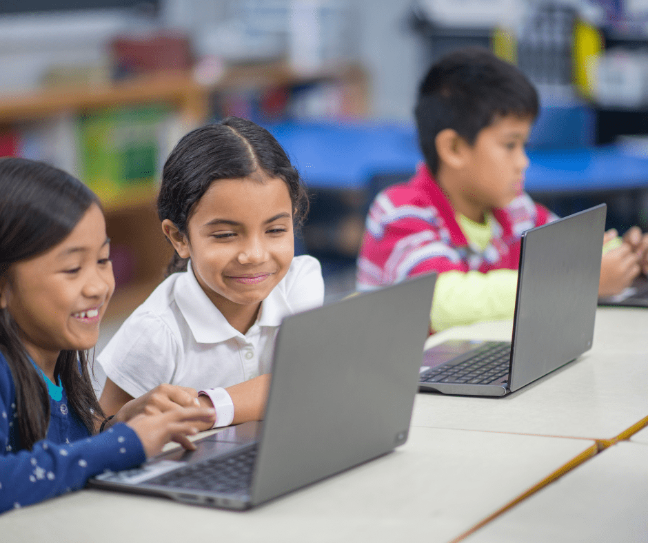 children sit at table working on laptops