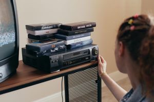 woman looks at DVD player topped with a stack of DVDs